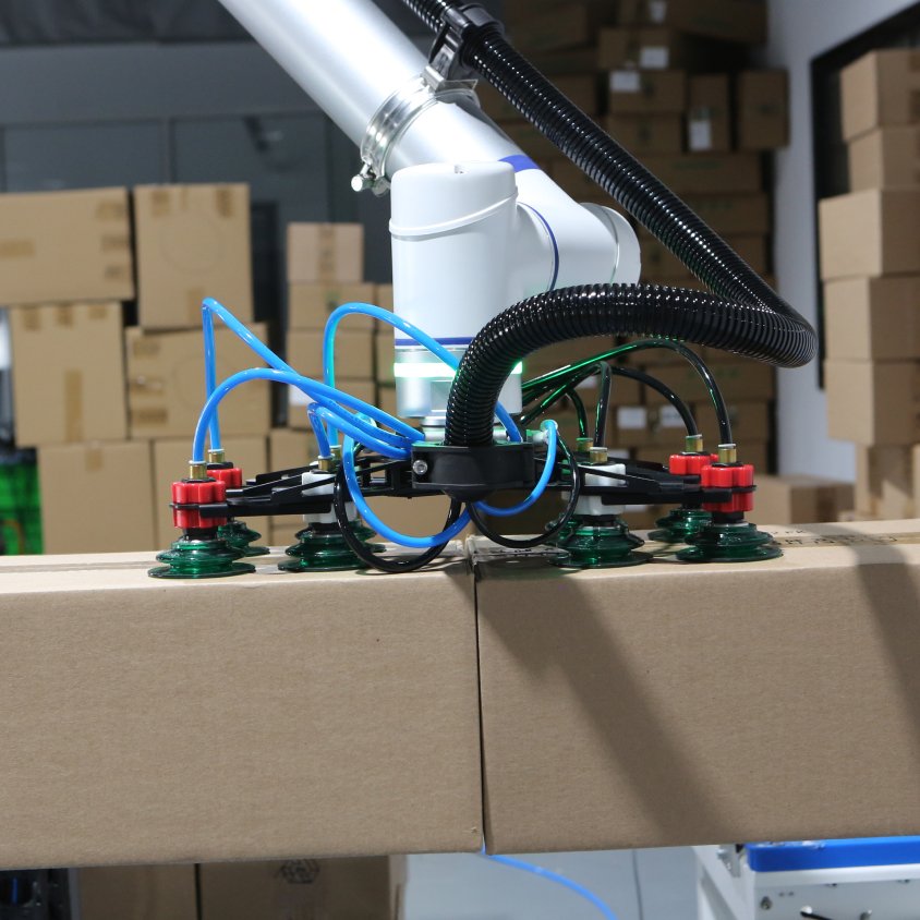 Gripper con ventosas de vacío de un robot colaborativo de paletizado levantando cajas de cartón.
